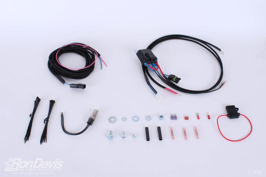 An automotive wiring harness kit laid out on a white background, including a main black harness with multi-colored wires, a smaller black wire bundle, zip ties, a U-bend wire, mounting hardware, and a red wire connector. A RonDavis logo watermark is visible in the bottom-left corner.